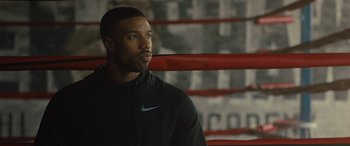 Movie still from “Creed II” (2018), directed by Steven Caple Jr. – A man sitting in a boxing ring wearing a black jacket; Close Up shot, Over the shoulder angle