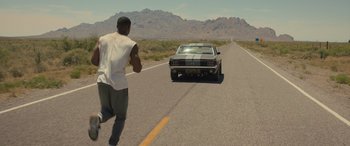Movie still from “Creed II” (2018), directed by Steven Caple Jr. – A man running down the middle of the road towards a car; Wide shot, High angle