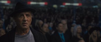 Movie still from “Creed II” (2018), directed by Steven Caple Jr. – A crowd of people are standing in front of a microphone; Close Up shot, Over the shoulder angle