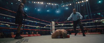 Movie still from “Creed II” (2018), directed by Steven Caple Jr. – A man laying on the ground in a boxing ring; Wide shot, High angle