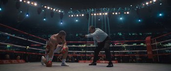 Movie still from “Creed II” (2018), directed by Steven Caple Jr. – A referee and a man in a boxing ring; Wide shot, Over the shoulder angle
