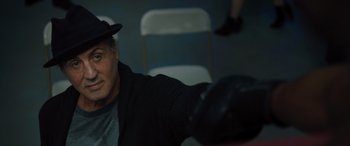 Movie still from “Creed II” (2018), directed by Steven Caple Jr. – An older man wearing a hat sitting on a chair; Close Up shot, Over the shoulder angle