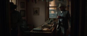 Movie still from “Cry Macho” (2021), directed by Clint Eastwood – A man standing in front of a table with papers on top of it; Wide shot, Over the shoulder angle