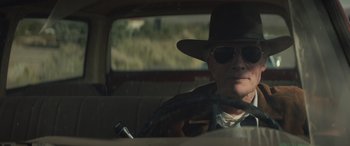 Movie still from “Cry Macho” (2021), directed by Clint Eastwood – An older man driving a car wearing a hat and sunglasses; Close Up shot, Low angle