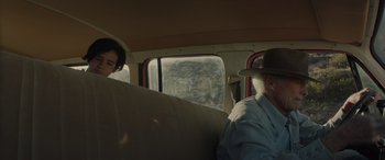 Movie still from “Cry Macho” (2021), directed by Clint Eastwood – An older man and a young woman sitting in the back of a car; Medium shot, Over the shoulder angle