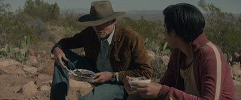 Movie still from “Cry Macho” (2021), directed by Clint Eastwood – A man sitting on the ground while holding a plate; Medium shot, Over the shoulder angle