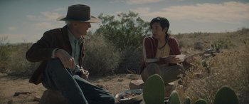 Movie still from “Cry Macho” (2021), directed by Clint Eastwood – Two men sitting on the ground in the desert; Medium shot, Over the shoulder angle