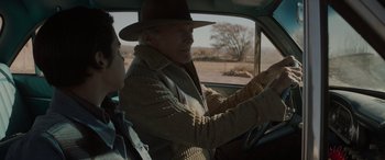 Movie still from “Cry Macho” (2021), directed by Clint Eastwood – An older man driving a car while a younger man watches; Medium shot, Over the shoulder angle