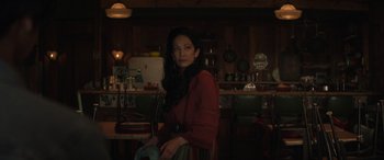 Movie still from “Cry Macho” (2021), directed by Clint Eastwood – A woman sitting in a chair in front of a counter; Medium shot, Over the shoulder angle