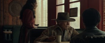 Movie still from “Cry Macho” (2021), directed by Clint Eastwood – An older man sitting at a table with a cup of coffee; Medium shot, Over the shoulder angle