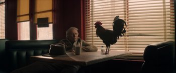 Movie still from “Cry Macho” (2021), directed by Clint Eastwood – An old woman sitting at a table with a glass of milk; Medium shot, Low angle