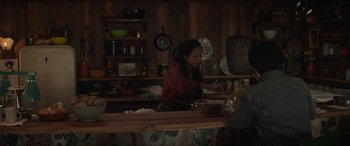 Movie still from “Cry Macho” (2021), directed by Clint Eastwood – A woman is preparing food in a wooden kitchen; Medium shot, Over the shoulder angle