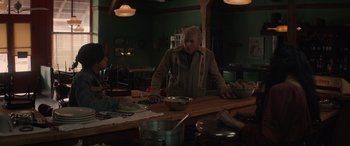 Movie still from “Cry Macho” (2021), directed by Clint Eastwood – A man standing at a table with a bowl of food on top of it; Medium shot, Over the shoulder angle