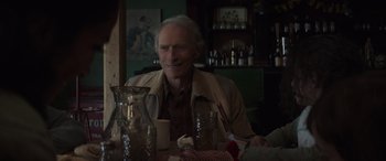 Movie still from “Cry Macho” (2021), directed by Clint Eastwood – An older man sitting at a table with a glass of water; Medium shot, Over the shoulder angle