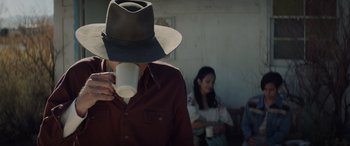 Movie still from “Cry Macho” (2021), directed by Clint Eastwood – A man in a hat drinking a cup of coffee while a woman watches; Medium shot, Over the shoulder angle