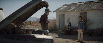 Movie still from “Cry Macho” (2021), directed by Clint Eastwood – An older man standing in front of an open car hood; Wide shot, Over the shoulder angle