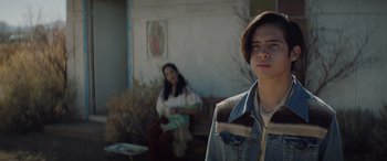 Movie still from “Cry Macho” (2021), directed by Clint Eastwood – A man and a woman sitting in front of a building; Medium shot, Over the shoulder angle