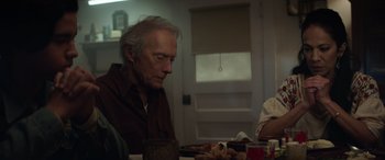 Movie still from “Cry Macho” (2021), directed by Clint Eastwood – An older man sitting at a dinner table with food; Medium shot, Over the shoulder angle