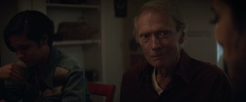 Movie still from “Cry Macho” (2021), directed by Clint Eastwood – An older man sitting at a table in front of a red chair; Close Up shot, Over the shoulder angle