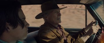 Movie still from “Cry Macho” (2021), directed by Clint Eastwood – An older man wearing a hat sitting in the back of a car; Close Up shot, Over the shoulder angle