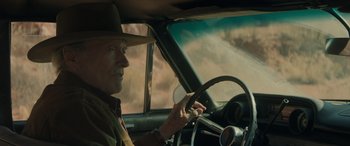 Movie still from “Cry Macho” (2021), directed by Clint Eastwood – A man in a hat driving a car in the desert; Medium shot, Over the shoulder angle