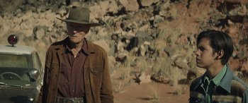 Movie still from “Cry Macho” (2021), directed by Clint Eastwood – An older man wearing a hat standing in front of rocks; Medium shot, Over the shoulder angle