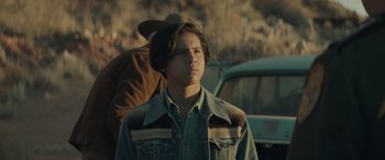 Movie still from “Cry Macho” (2021), directed by Clint Eastwood – A young man standing in front of some cars; Medium shot, Over the shoulder angle