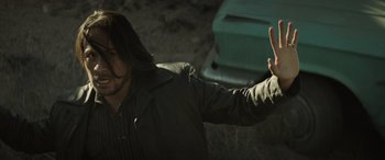 Movie still from “Cry Macho” (2021), directed by Clint Eastwood – A man with long black hair is holding a gun; Medium shot, Over the shoulder angle
