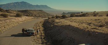 Movie still from “Cry Macho” (2021), directed by Clint Eastwood – A man standing on the side of a road next to a car; Extreme Wide shot, High angle