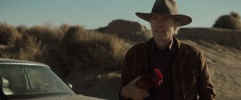 Movie still from “Cry Macho” (2021), directed by Clint Eastwood – An older man holding a chicken in his hand; Close Up shot, Over the shoulder angle