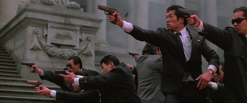 Movie still from “Crying Freeman” (1995), directed by Christophe Gans – A group of men in suits holding guns in their hands; Medium shot, Low angle