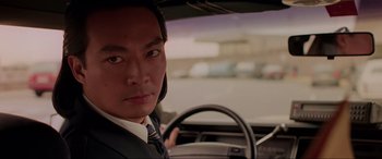 Movie still from “Crying Freeman” (1995), directed by Christophe Gans – A man in a suit sitting in the driver's seat of a car; Close Up shot, Low angle