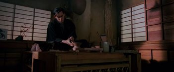 Movie still from “Crying Freeman” (1995), directed by Christophe Gans – A man in a black shirt is working on a bowl; Medium shot, Low angle