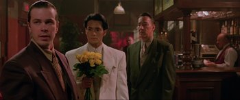 Movie still from “Crying Freeman” (1995), directed by Christophe Gans – A man holding a bouquet of yellow roses in front of another man; Medium shot, Over the shoulder angle
