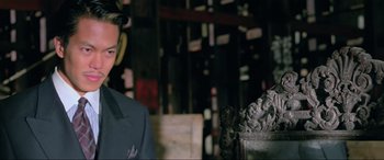 Movie still from “Crying Freeman” (1995), directed by Christophe Gans – A man standing next to a statue in a room; Close Up shot, Over the shoulder angle