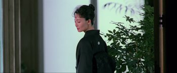 Movie still from “Crying Freeman” (1995), directed by Christophe Gans – A woman with a backpack is standing in front of a tree; Medium shot, Low angle