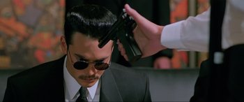 Movie still from “Crying Freeman” (1995), directed by Christophe Gans – A man in a suit and sunglasses holding a gun; Close Up shot, High angle