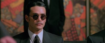 Movie still from “Crying Freeman” (1995), directed by Christophe Gans – A person wearing a suit and sunglasses; Close Up shot, Low angle