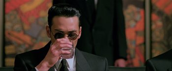 Movie still from “Crying Freeman” (1995), directed by Christophe Gans – A man in a suit and tie drinking a glass of water; Close Up shot, High angle