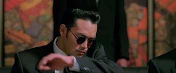 Movie still from “Crying Freeman” (1995), directed by Christophe Gans – A person wearing a suit and sunglasses; Close Up shot, Low angle