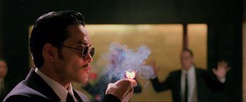 Movie still from “Crying Freeman” (1995), directed by Christophe Gans – A man in sunglasses holding a burning match; Close Up shot, Low angle