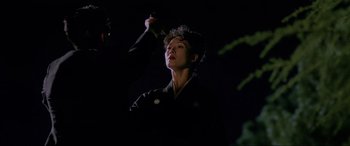 Movie still from “Crying Freeman” (1995), directed by Christophe Gans – A woman is holding something up to her face in the dark; Medium shot, Low angle