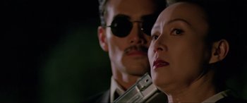 Movie still from “Crying Freeman” (1995), directed by Christophe Gans – A man and a woman holding a gun in front of a wall; Close Up shot, Low angle