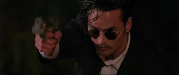 Movie still from “Crying Freeman” (1995), directed by Christophe Gans – A person holding a gun wearing sunglasses; Close Up shot, Low angle