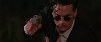 Movie still from “Crying Freeman” (1995), directed by Christophe Gans – A man in a suit and sunglasses holding a gun; Close Up shot, Low angle