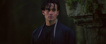 Movie still from “Crying Freeman” (1995), directed by Christophe Gans – A young man with long black hair wearing a black jacket; Close Up shot, Low angle