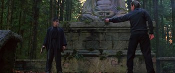 Movie still from “Crying Freeman” (1995), directed by Christophe Gans – A man standing in front of a statue pointing a gun at another man; Wide shot, Low angle