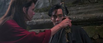 Movie still from “Crying Freeman” (1995), directed by Christophe Gans – A man holding a sword in front of a woman; Close Up shot, Low angle