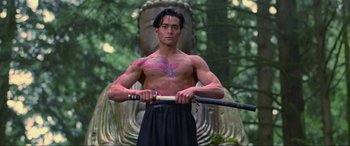 Movie still from “Crying Freeman” (1995), directed by Christophe Gans – A man holding a sword in front of a statue; Medium shot, Low angle