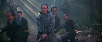Movie still from “Crying Freeman” (1995), directed by Christophe Gans – A group of people standing in the woods holding a sword; Medium shot, Over the shoulder angle